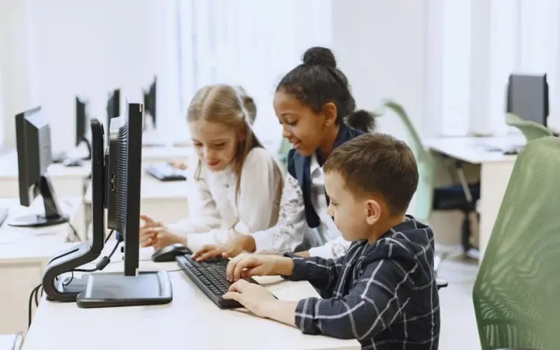 Photo of three kids coding together an a computer in a classroom