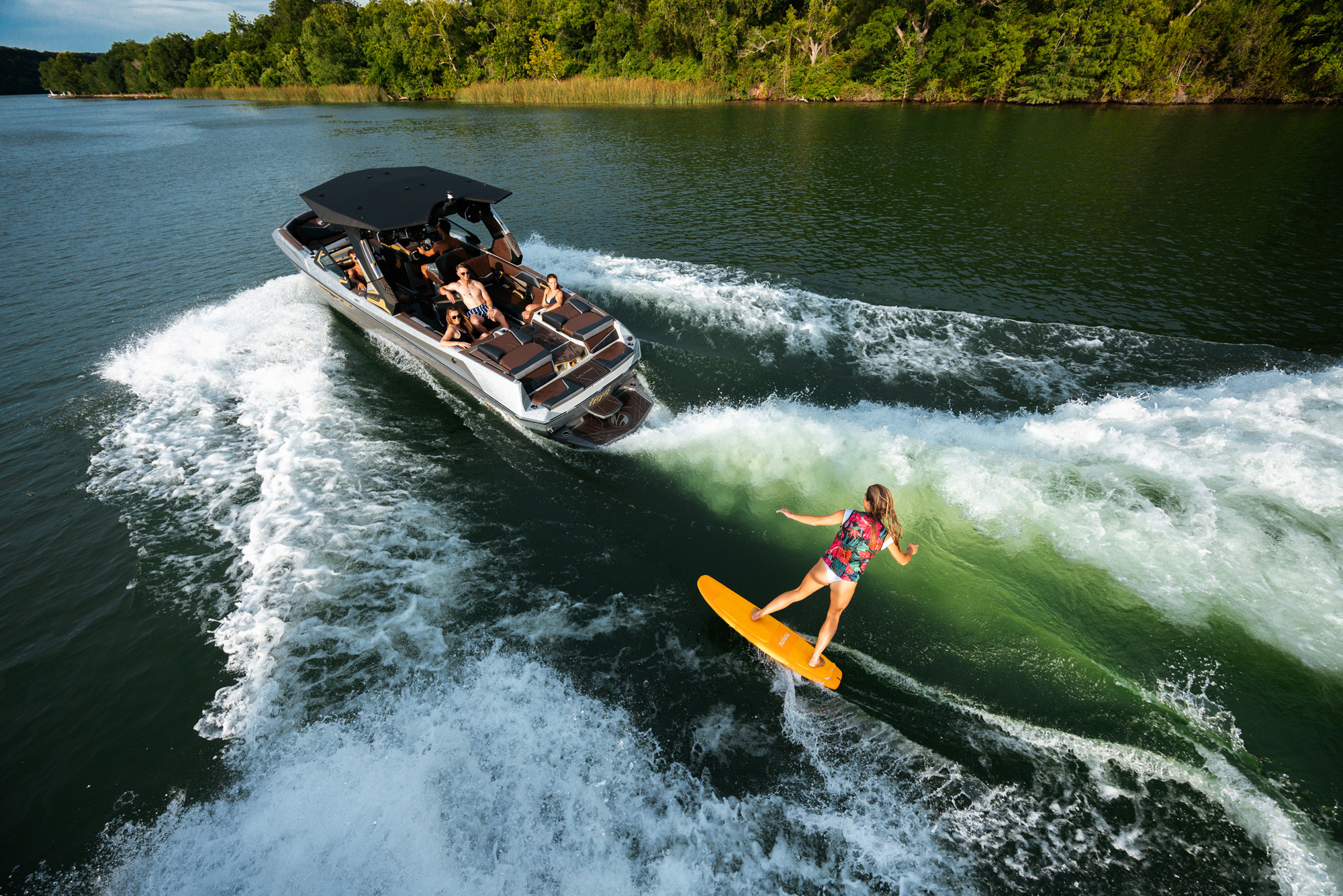 Person surfing on a yellow board behind a 2026 Tige Ultre 25ZX boat, wearing a colorful life vest, surrounded by splashing water.