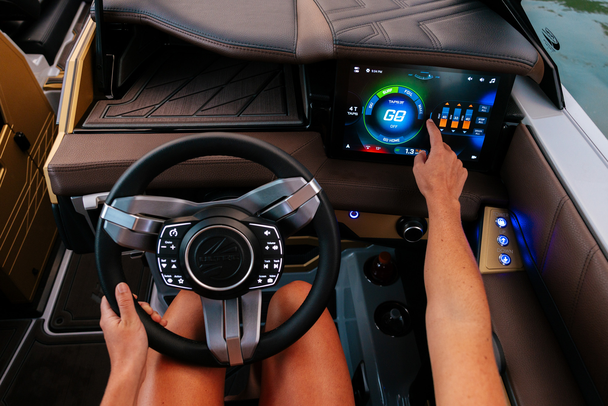 Person operating a modern 2026 Tige Ultre 25ZX boat dashboard with a touchscreen display and a steering wheel, featuring illuminated controls and a digital interface.