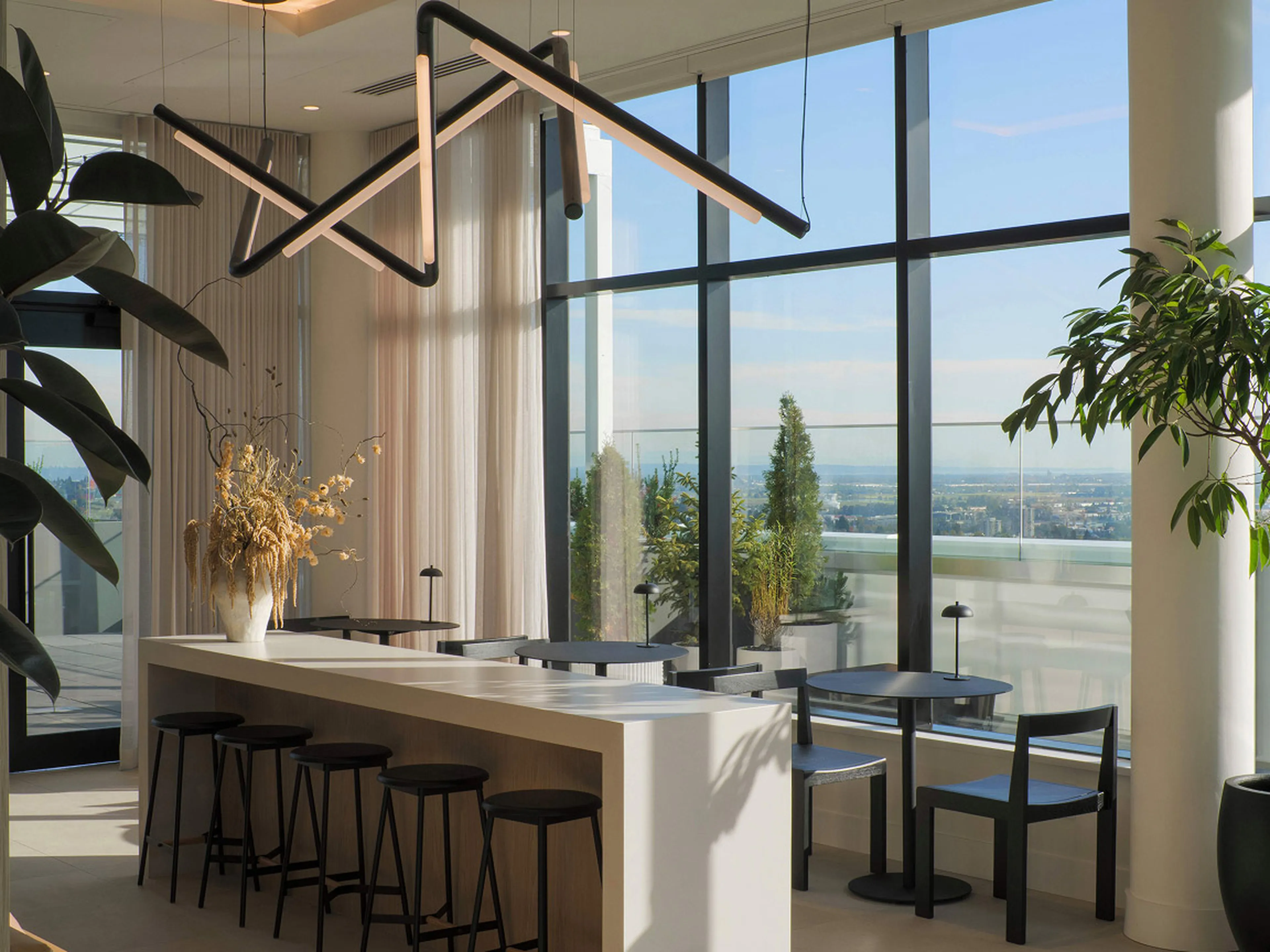 Modern interior with large windows, minimalistic black furniture, a long bar with stools, and geometric lighting. Outdoor view with plants visible.