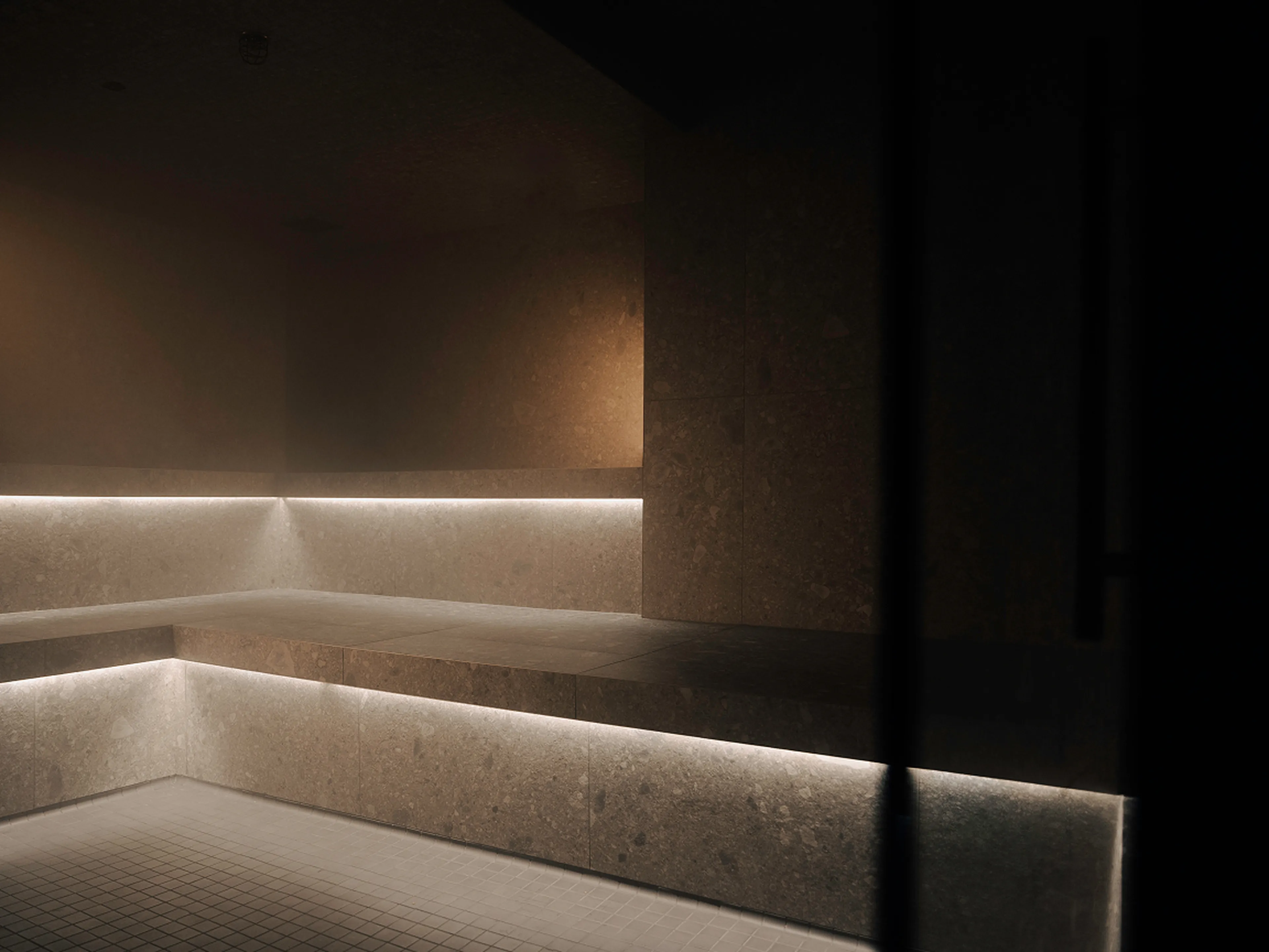 A dimly lit steam room with tiered stone seating and subtle under-seat lighting, creating a calm and serene atmosphere.