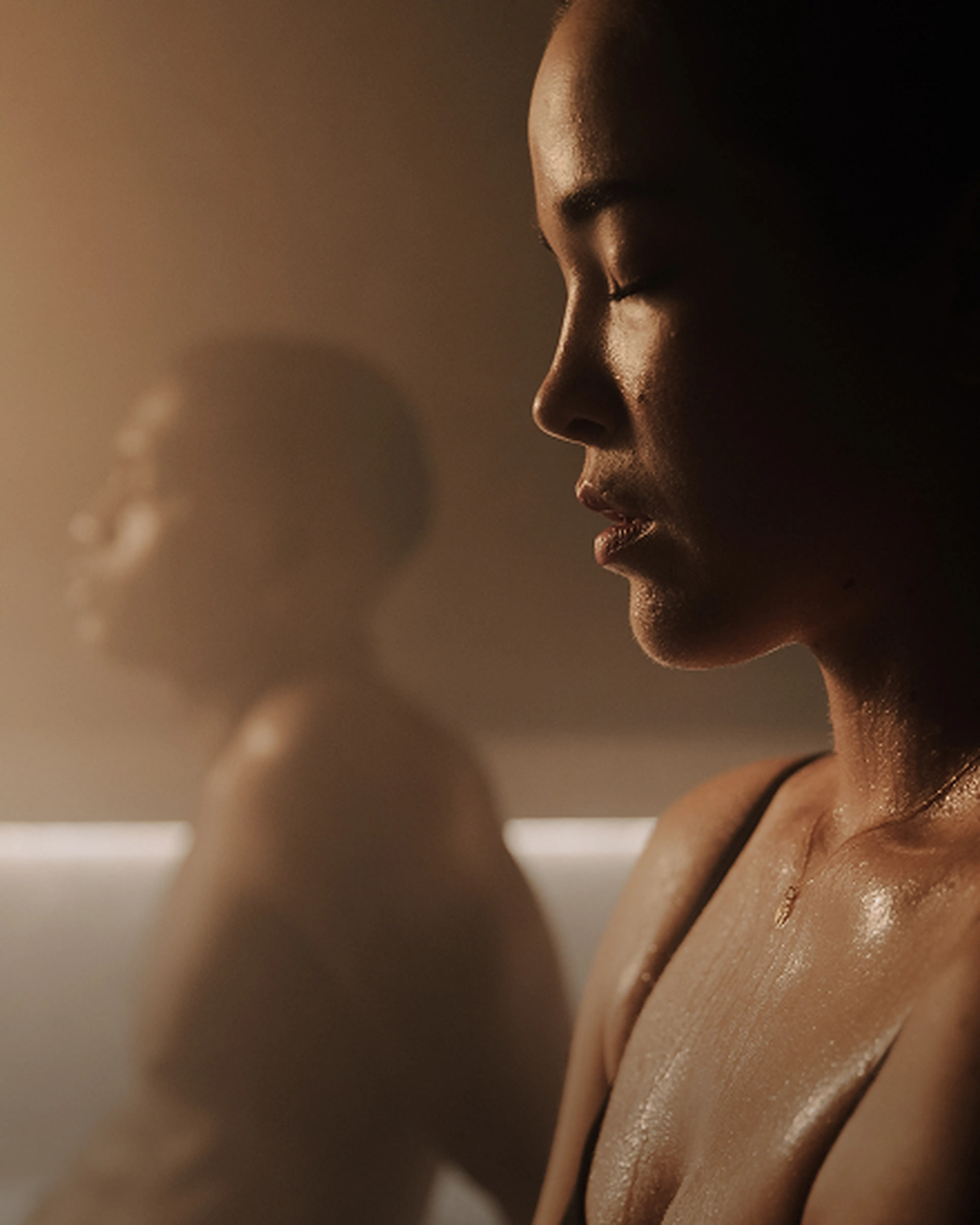 Two people in a dimly lit sauna, both appearing relaxed and sweating, one facing forward, the other in profile with eyes closed.