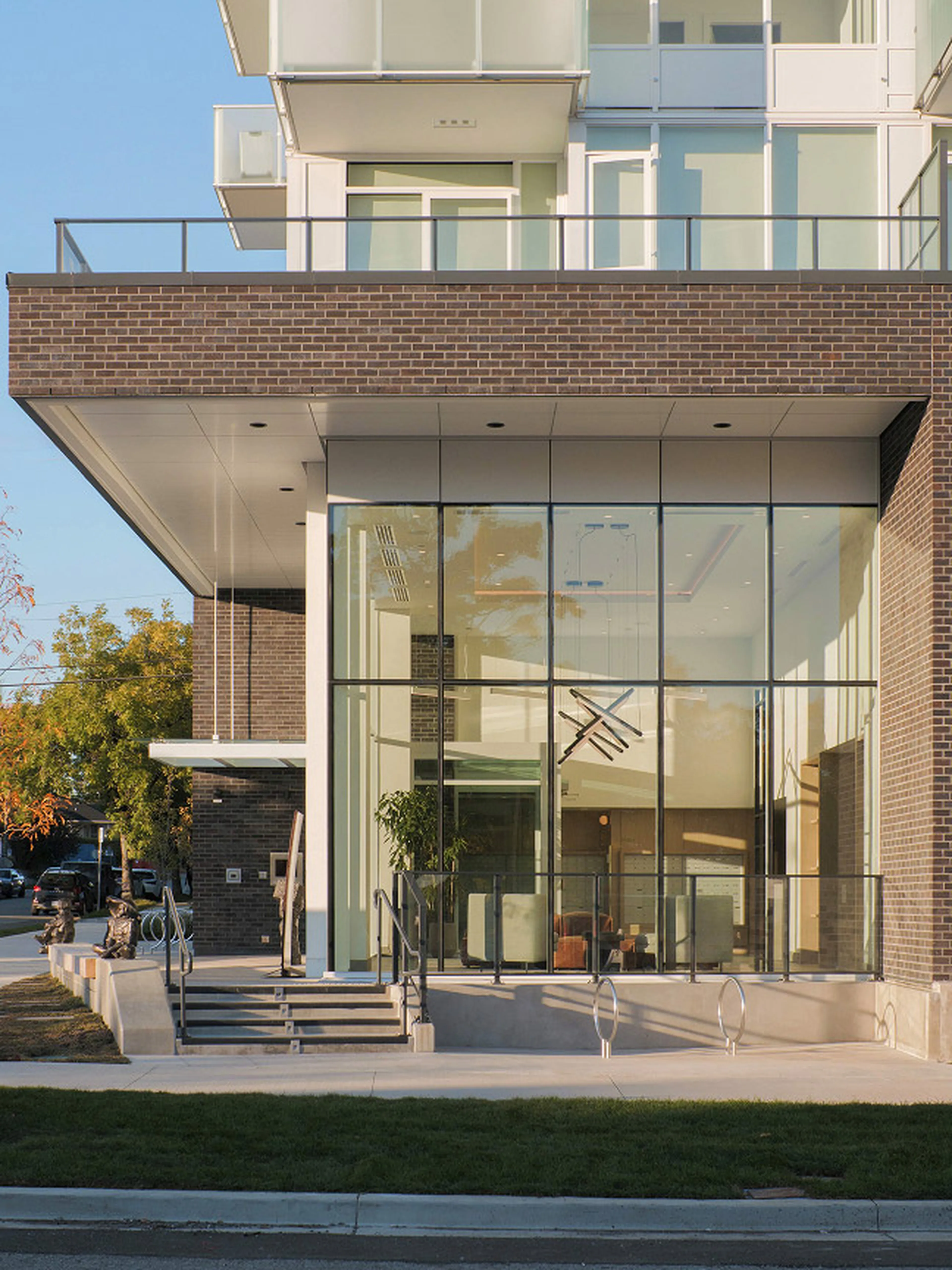 Modern building entrance with large glass windows, a black brick facade, steps leading up, and interior lighting visible.