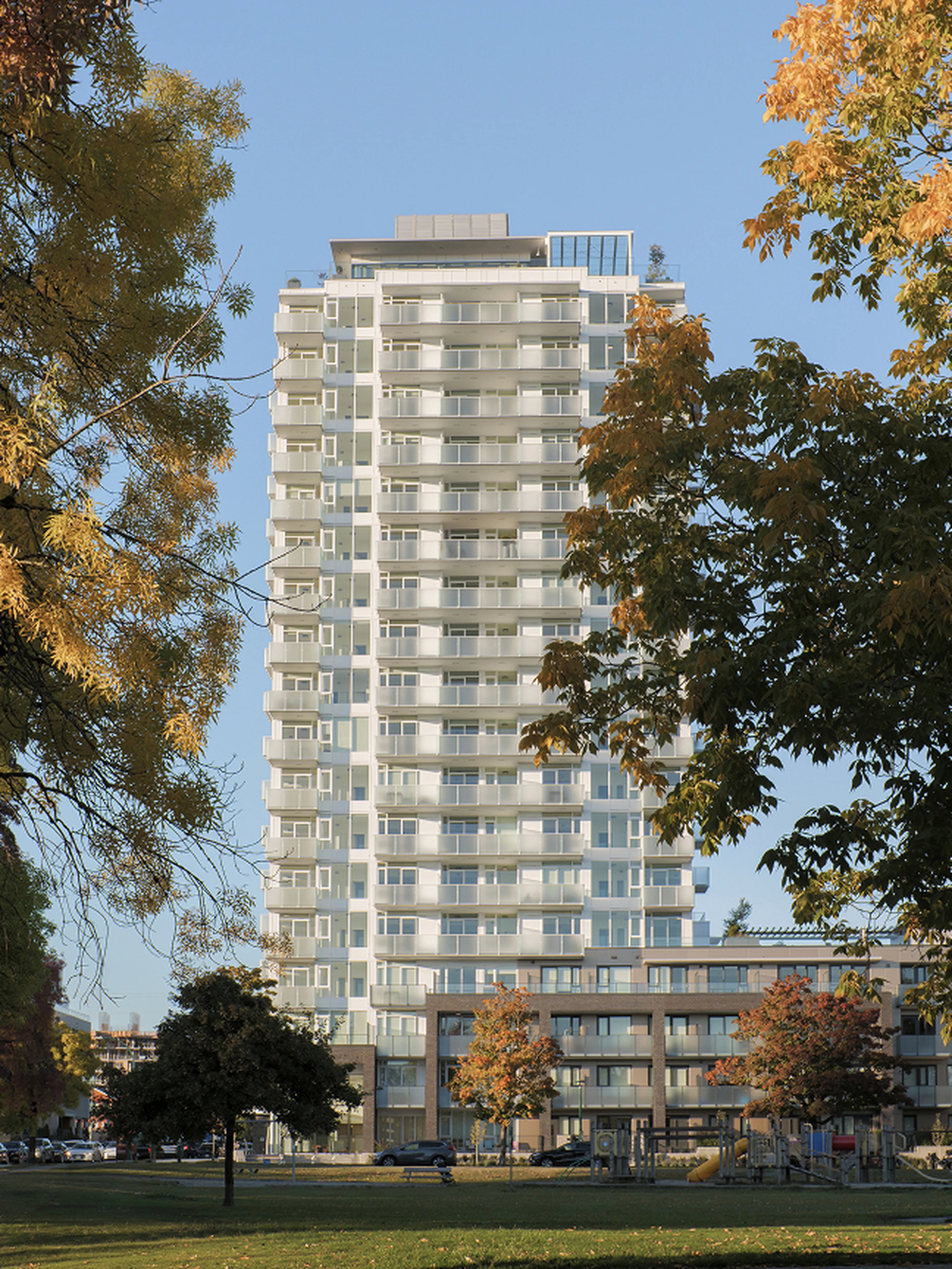 A tall modern apartment building surrounded by autumn trees with a clear blue sky in the background.