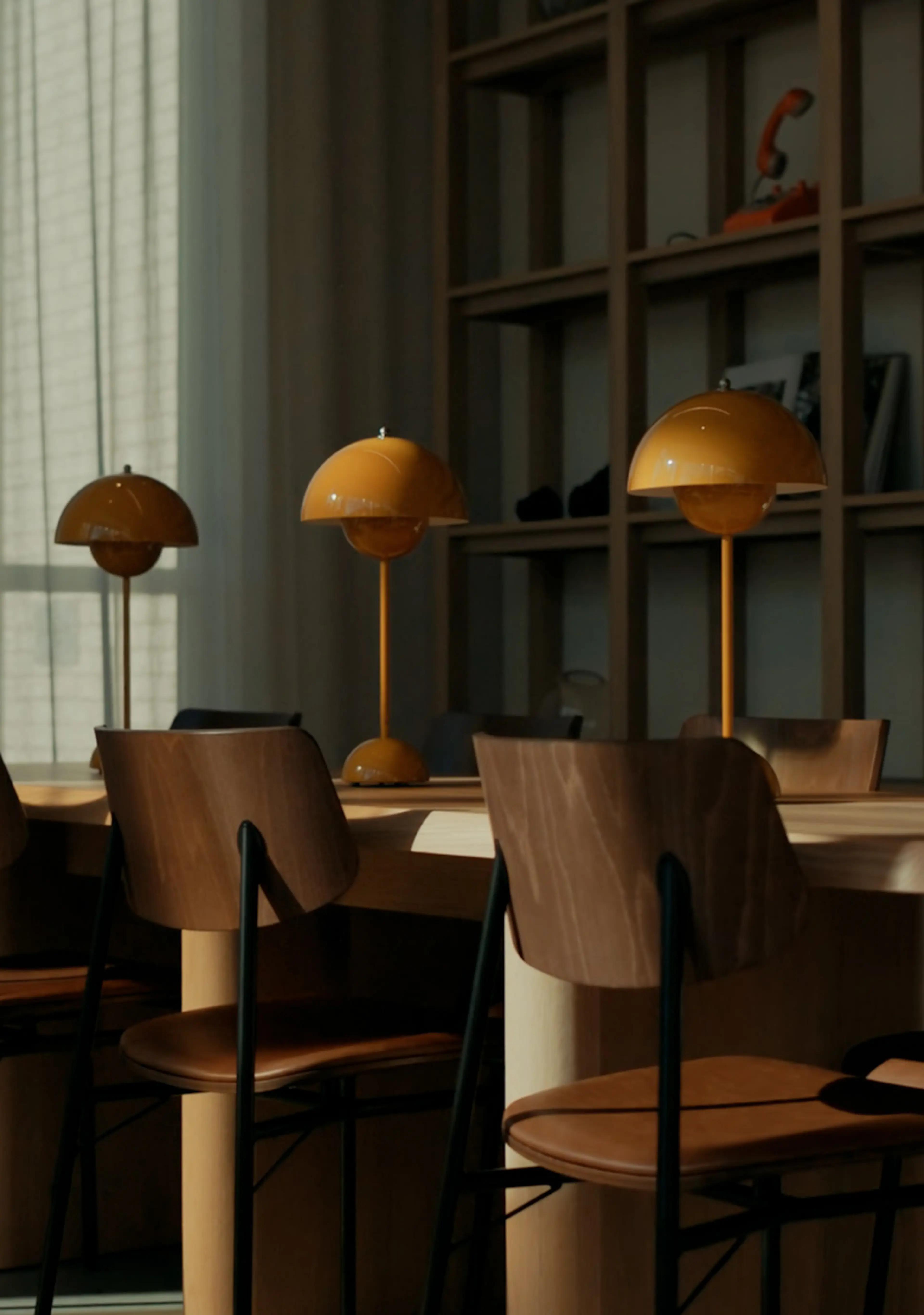 A modern lobby with wooden chairs, a long table, and four retro yellow lamps. Natural light filters through sheer curtains.