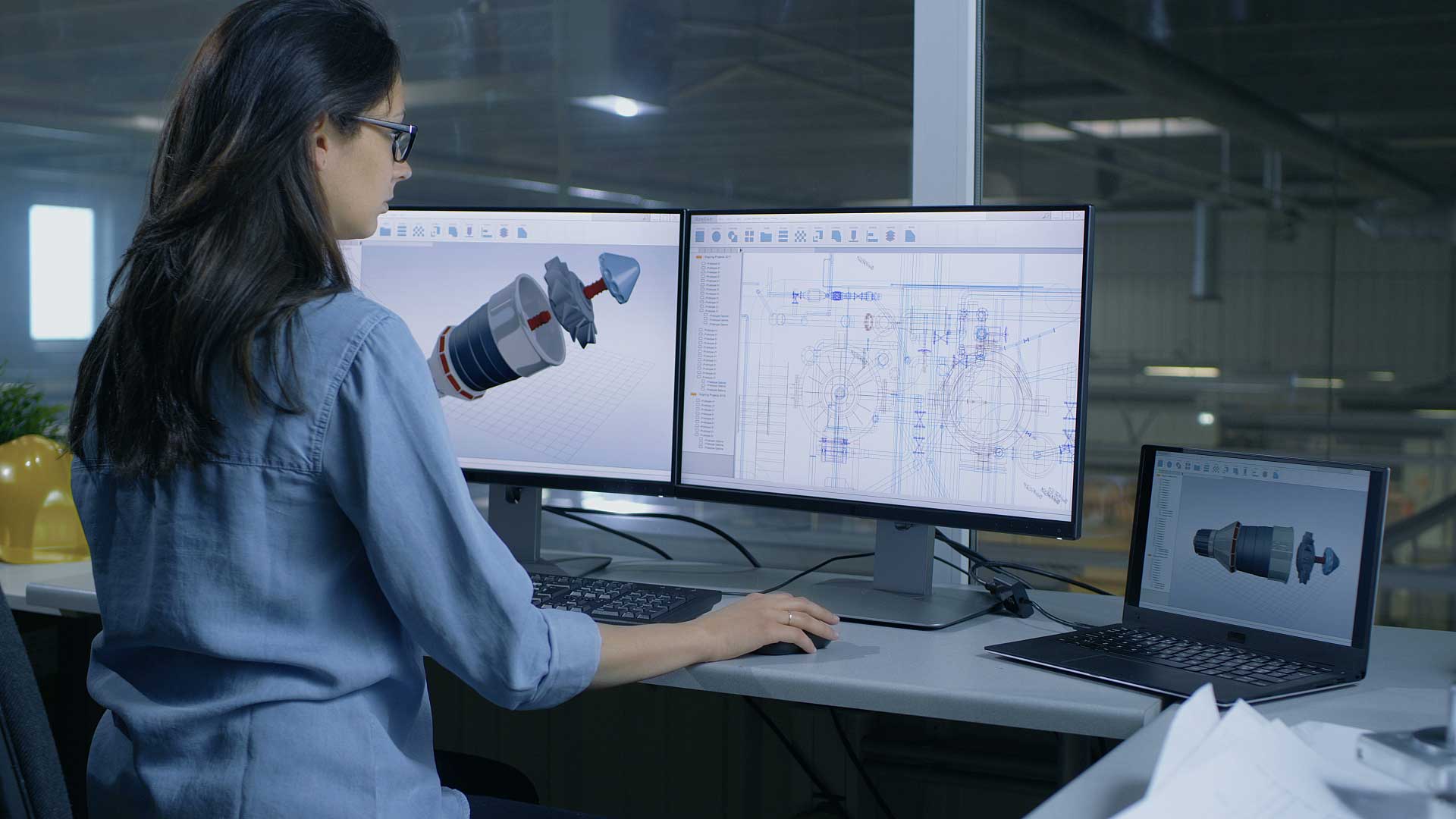 CAD engineer using CAD and PLM software with 3D and 2D data on multiple monitors.