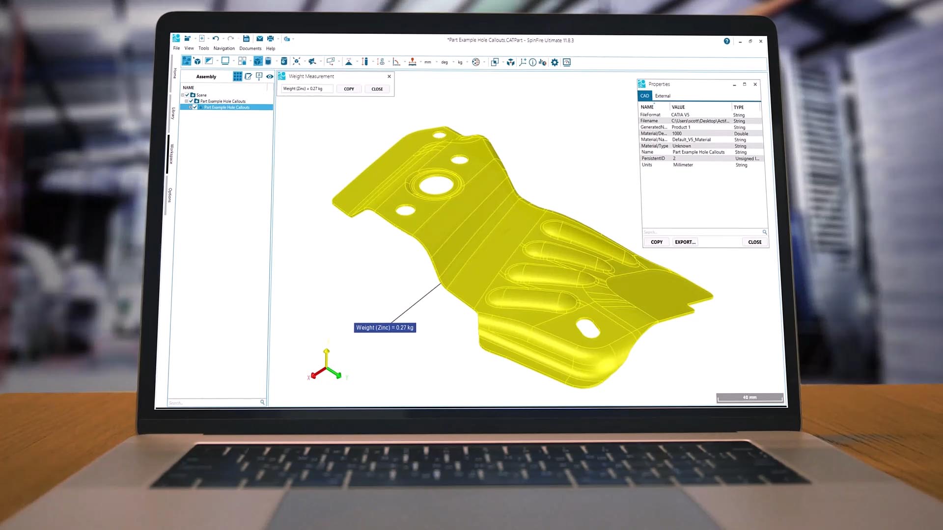 A laptop screen displaying 3D modeling software with a yellow mechanical part design and various toolbars and menus visible.