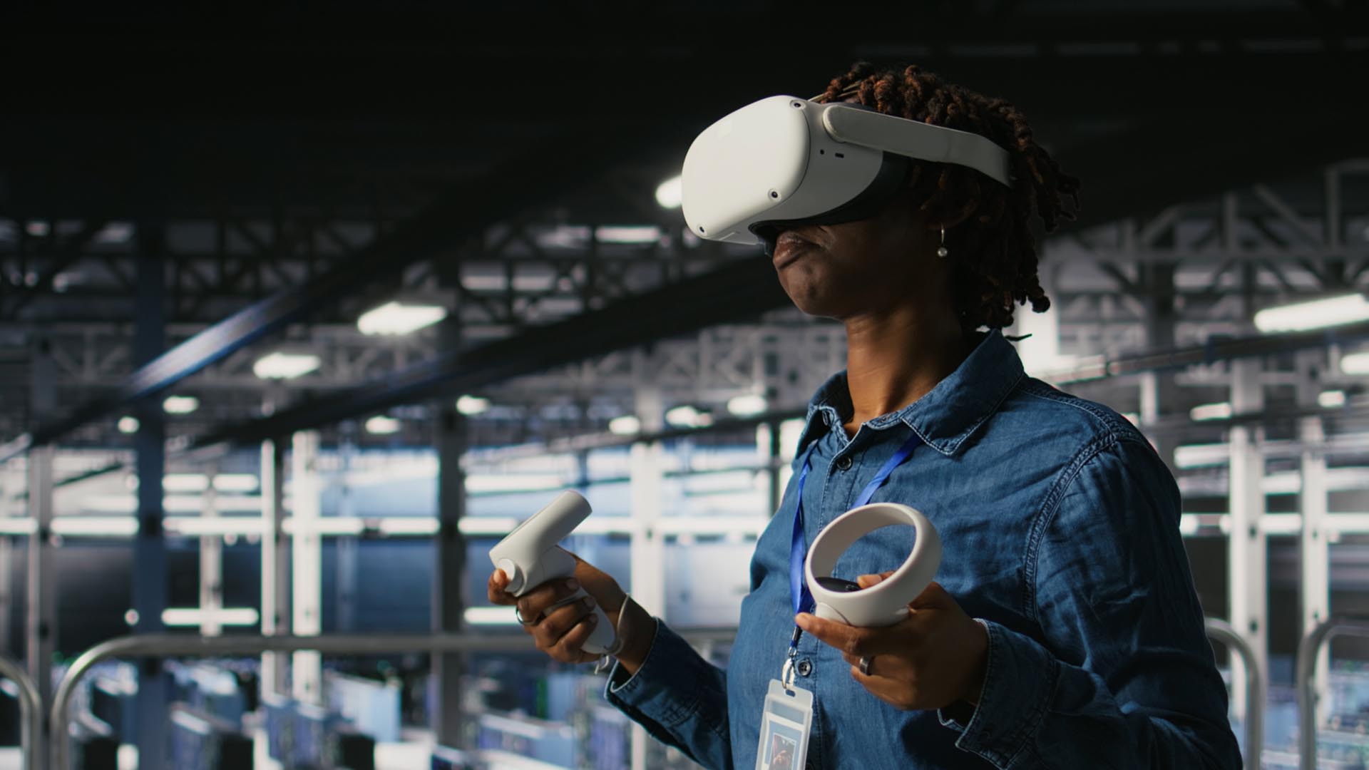 A woman wearing a virtual reality headset and holding controllers in a manufacturing environment.