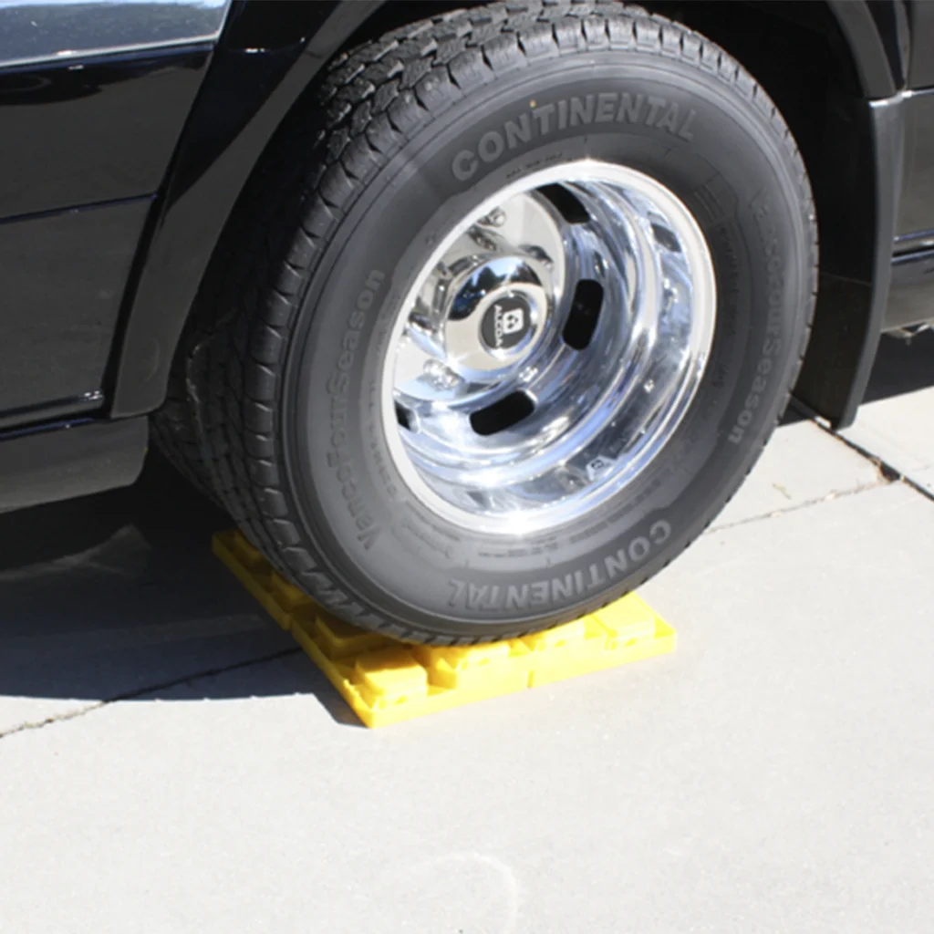 Car tire resting on a bright yellow wheel chock on a concrete surface, with a shiny chrome wheel rim visible.