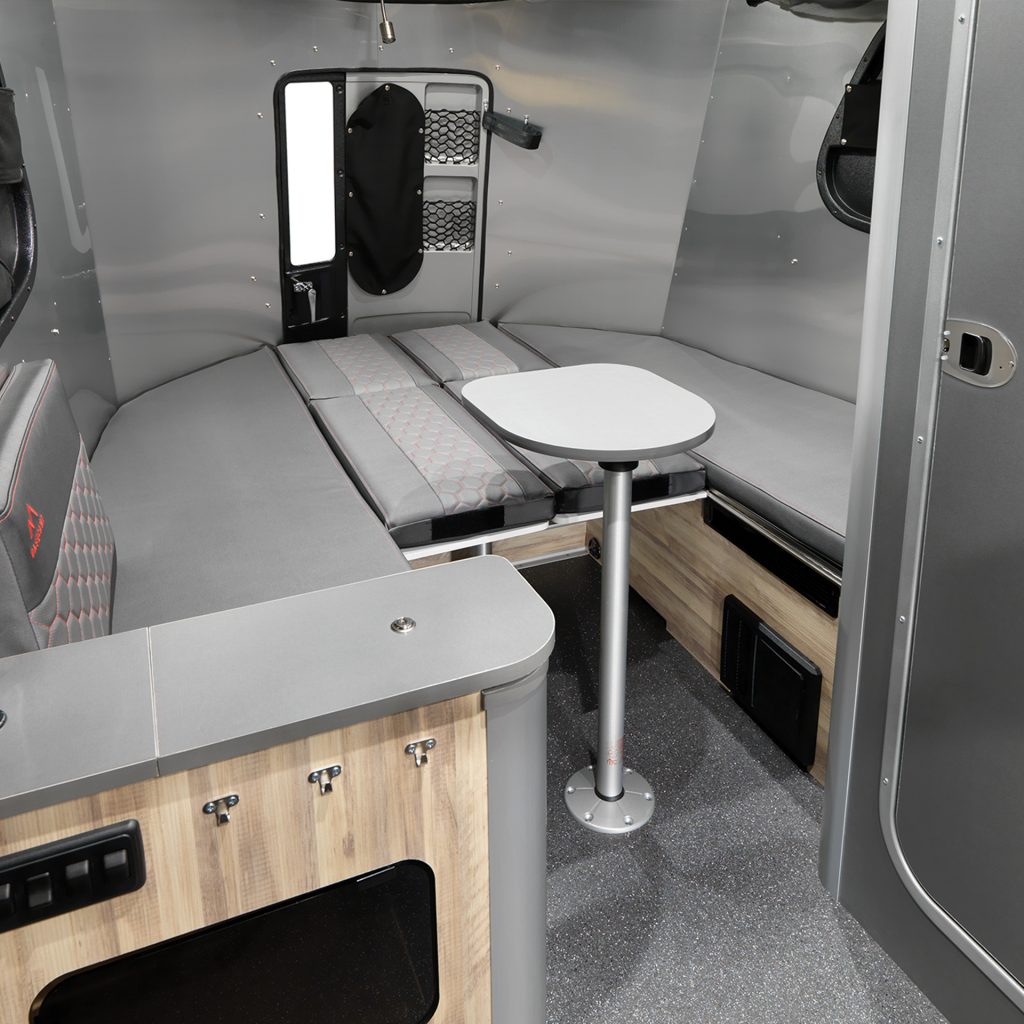 Interior of a compact camper van featuring a convertible seating area and table, with a modern gray and wood finish.