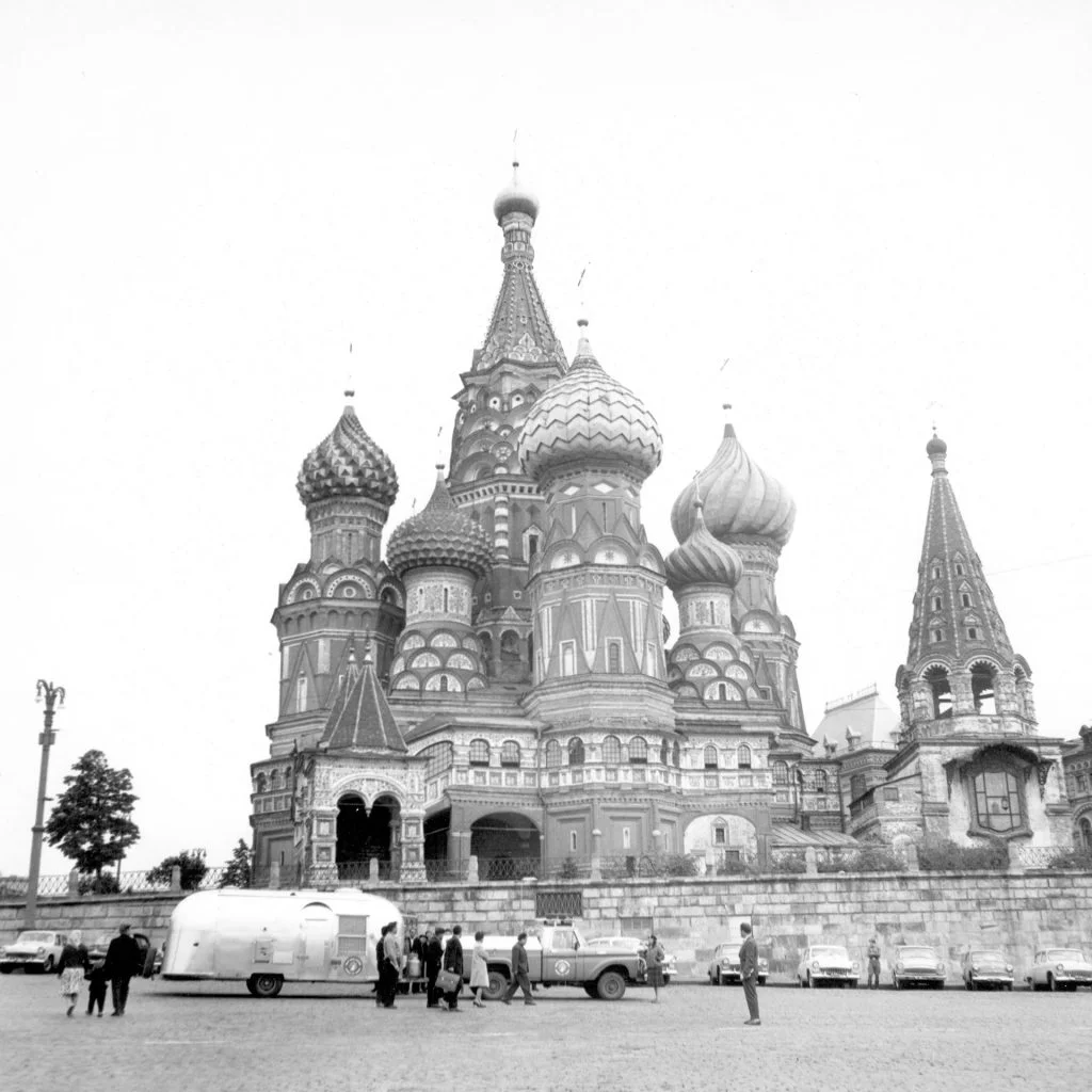 Black and white image of Saint Basil's Cathedral, with distinctive onion domes. People and vehicles are visible in the foreground.