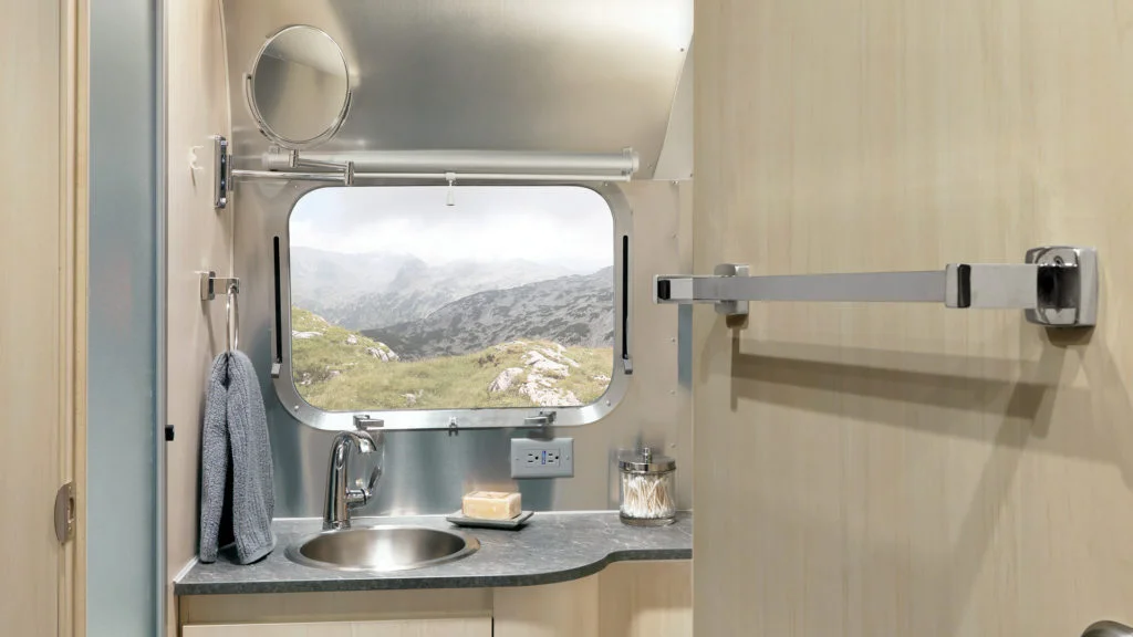 Campervan bathroom with a small sink, mirror, towel, and window showing a scenic mountain view.