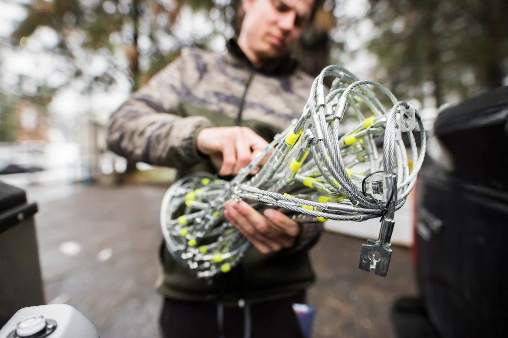 Person holding a coiled cable structure with yellow connectors, standing outside near some equipment.