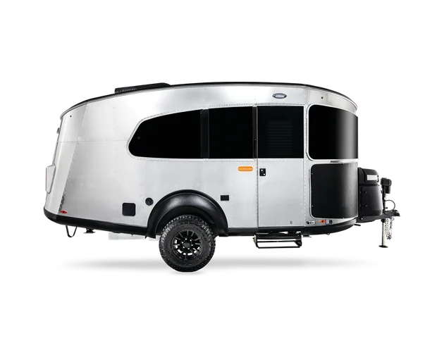 A sleek, silver modern travel trailer with a streamlined design, large black windows, and off-road tires on a white background.