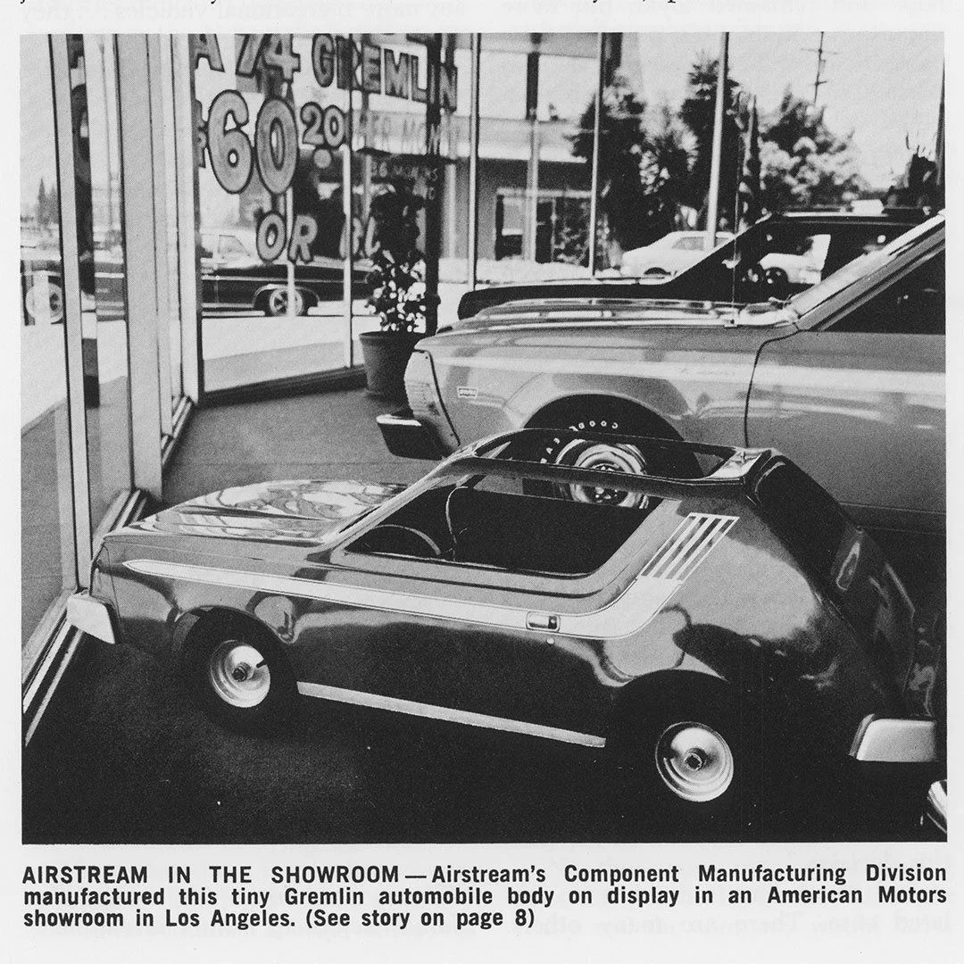 Tiny Gremlin car body displayed in a showroom, with another car partially visible, in a black and white photo.