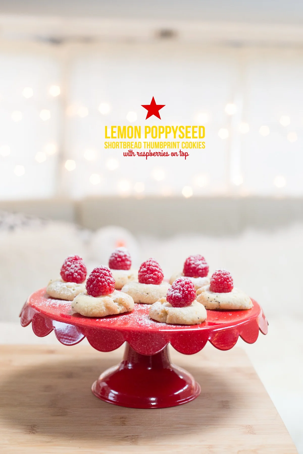 Cookies with raspberries on a red cake stand, titled "Lemon Poppyseed Shortbread Thumbprint Cookies," with bokeh lights in the background.