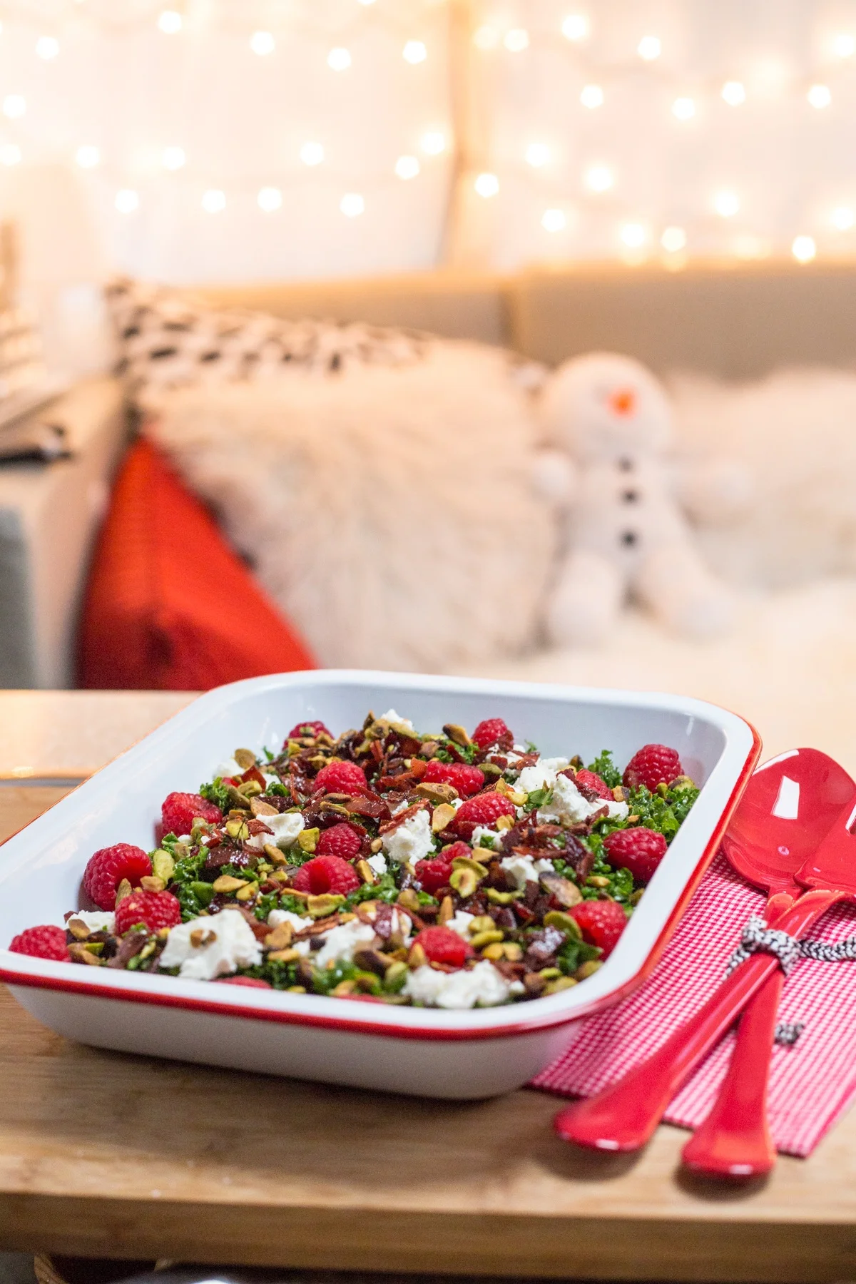 Festive salad with raspberries, goat cheese, nuts, and greens in a dish. Background with cozy lights and plush decor.