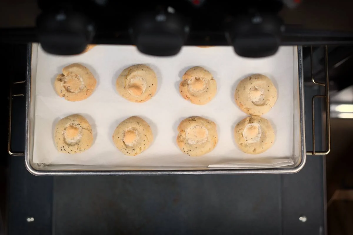 Eight round cookies baking on a parchment-lined tray in an oven, viewed from above.