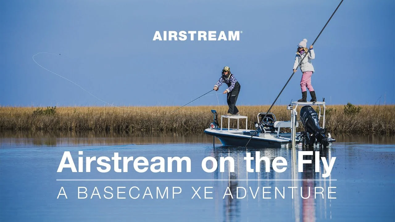 Two people fly fishing from a boat in a serene wetland, under a clear blue sky. Text: "Airstream on the Fly: A Basecamp XE Adventure."