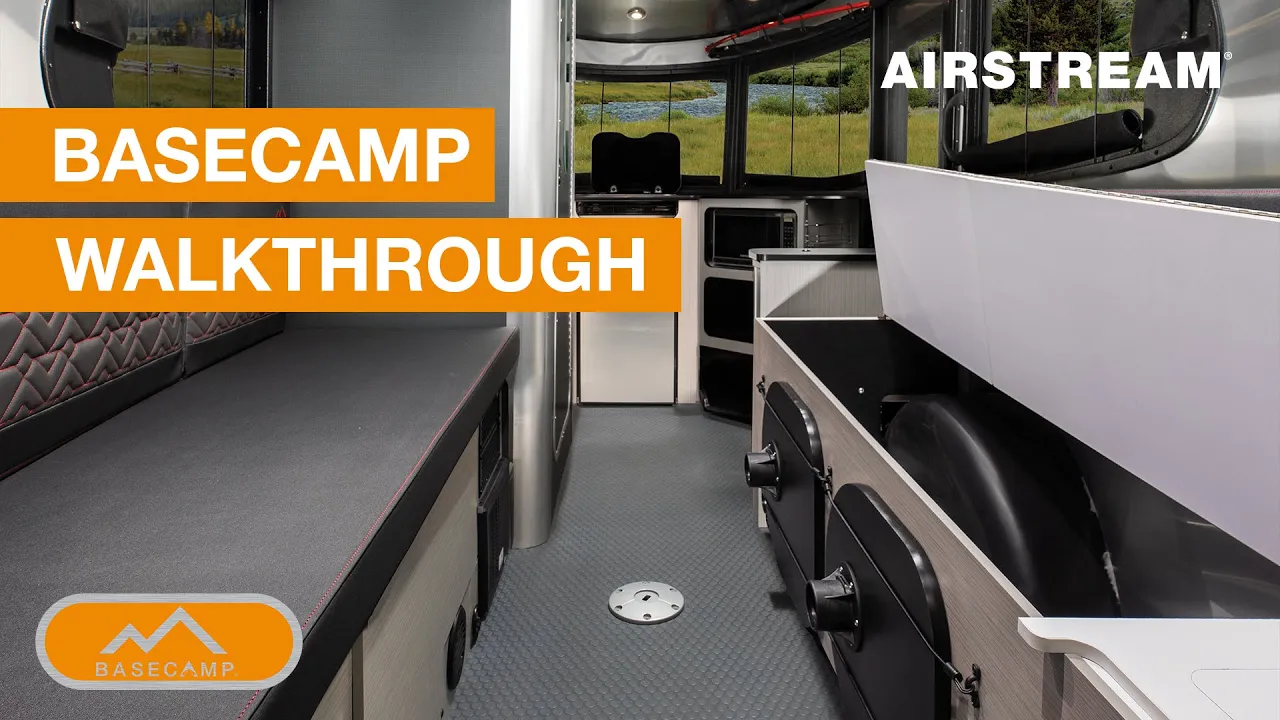 Interior view of an Airstream Basecamp, showing seating, storage compartments, and windows with a scenic outdoor view. Text overlay reads: "Basecamp Walkthrough".