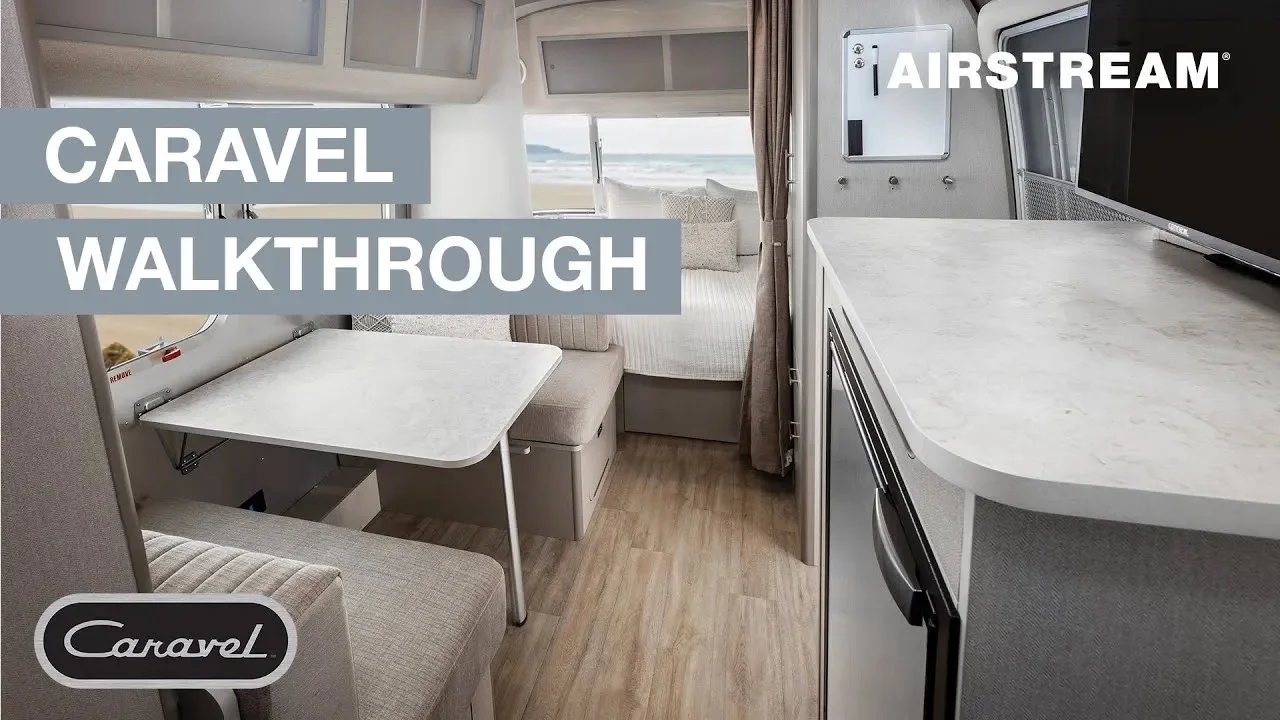 Interior view of an Airstream Caravel RV showing a kitchenette, dining area, and bed with a scenic ocean view. Text reads "Caravel Walkthrough."
