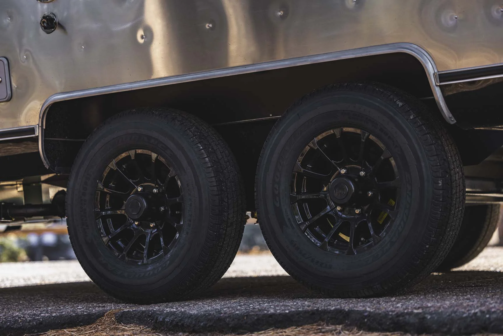 Close-up of black alloy wheels on a dual-axle trailer, with a silver metallic body in a sunlit outdoor setting.