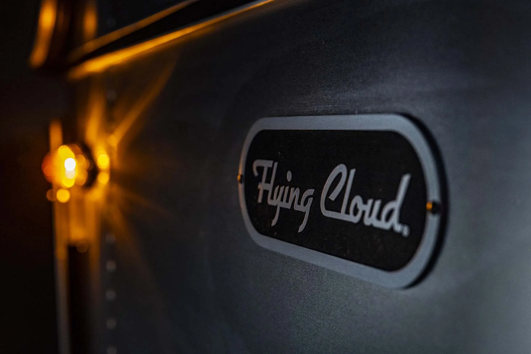 Close-up of a "Flying Cloud" logo on a dark surface, illuminated by a warm, glowing light on the left.