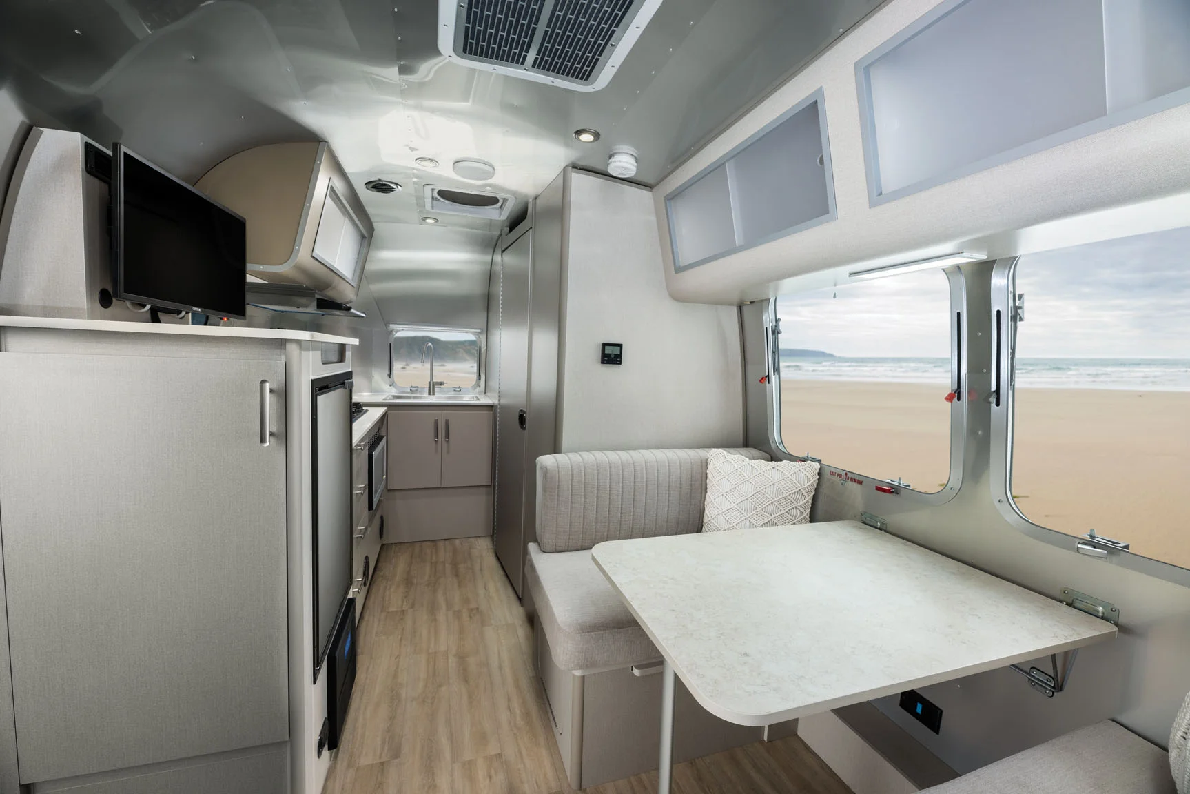 Modern RV interior featuring a compact kitchen and dining area with large windows overlooking a scenic beach.