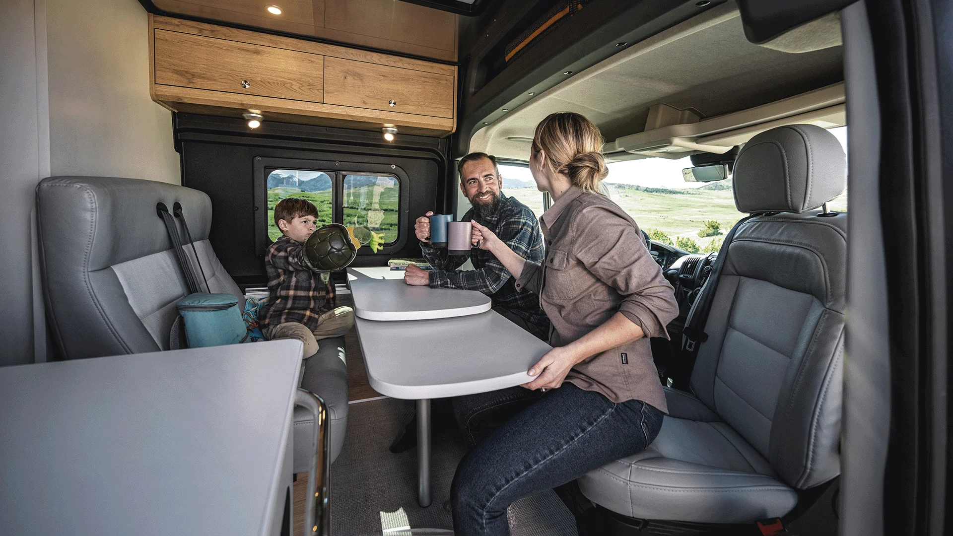 Family enjoying drinks and conversation inside a campervan with a foldable table, surrounded by scenic views outside the window.