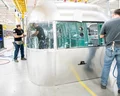 Workers assembling a shiny, silver trailer body in a well-lit factory, surrounded by tools and equipment.