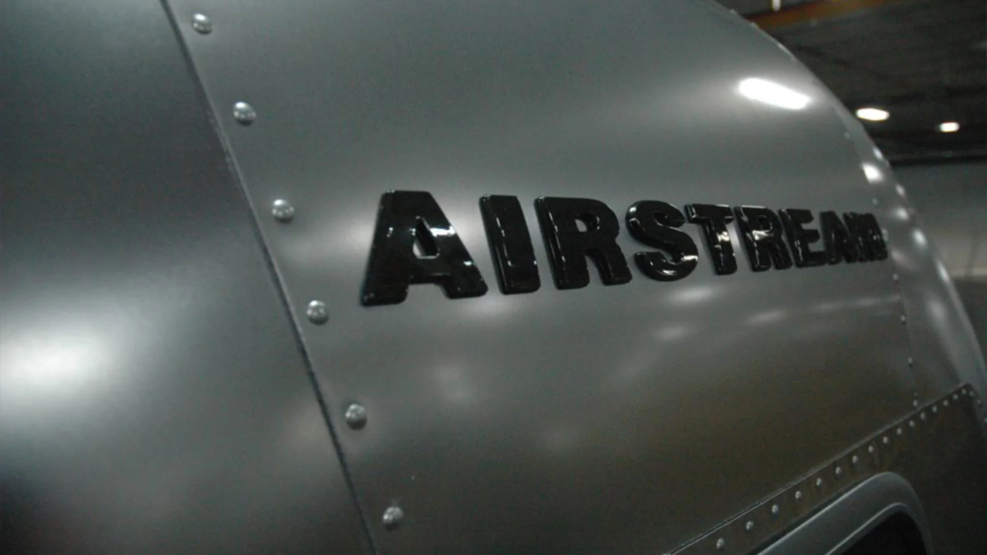 Close-up of metallic surface with the word "AIRSTREAM" in bold black letters, showing rivet details and industrial texture.