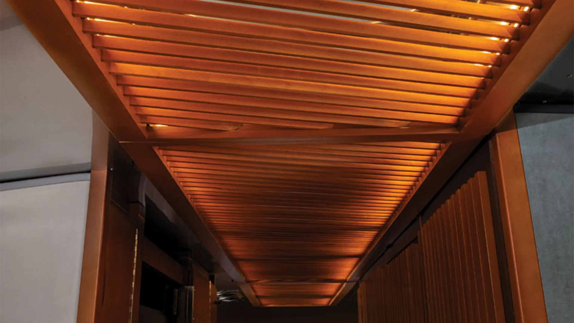 Wooden slatted ceiling with warm, ambient lighting casting a cozy glow, creating an inviting and modern architectural feature.