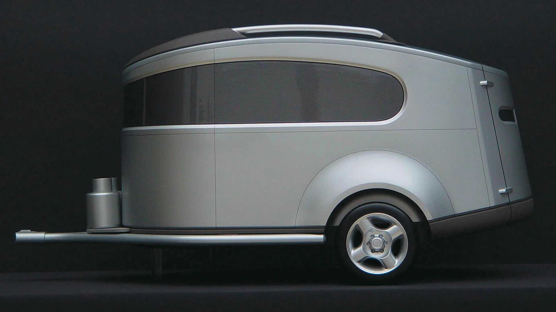 A sleek, futuristic silver trailer with curved windows and a rounded, aerodynamic design against a dark background.