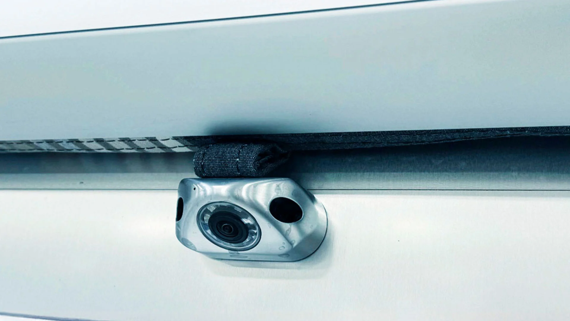 Close-up of a small security camera installed on a metallic surface, with wiring hidden by a fabric sleeve.