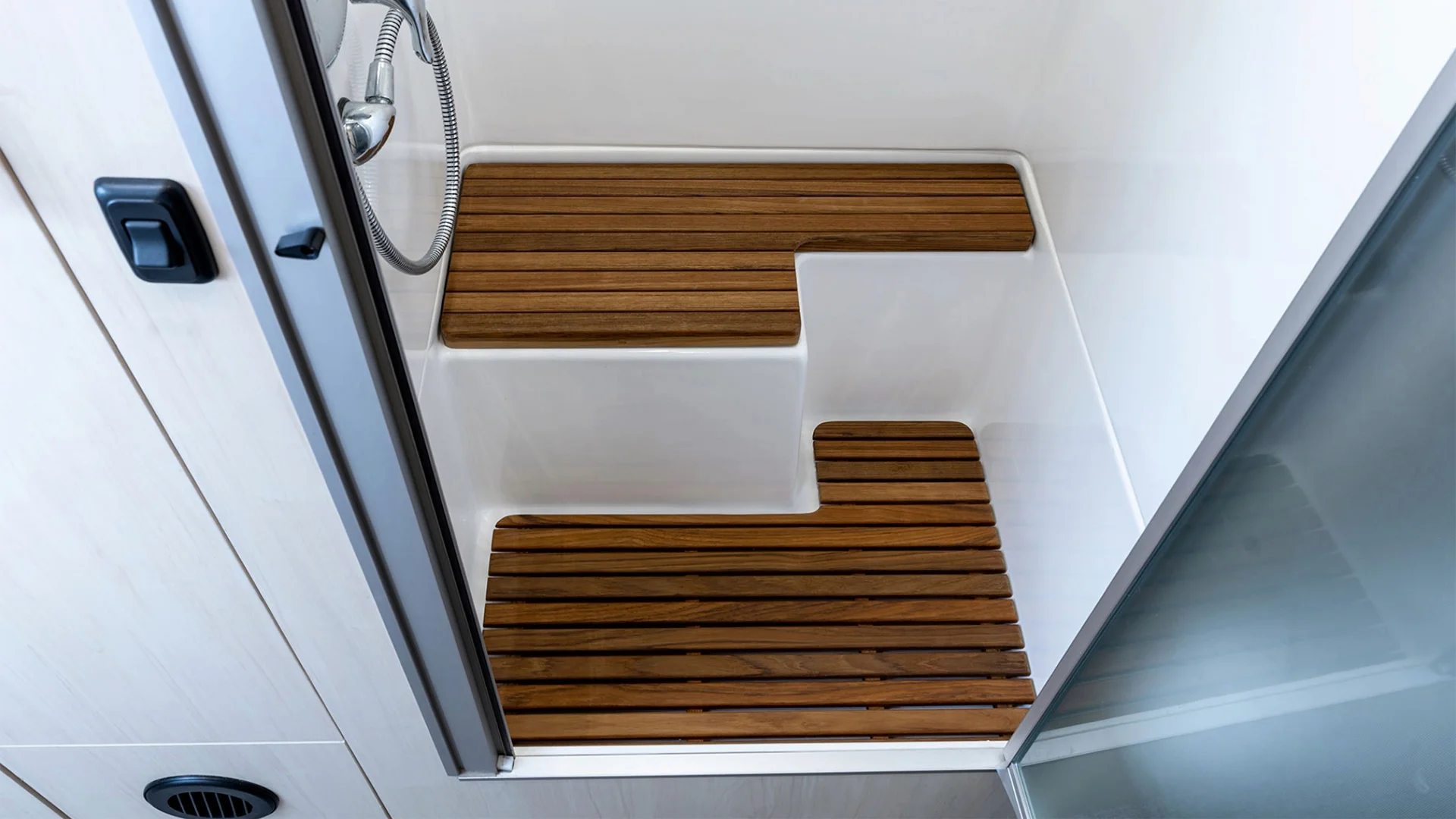 Small modern shower stall with wood-style slatted floor panels, white walls, and a sliding glass door, featuring a handheld showerhead.