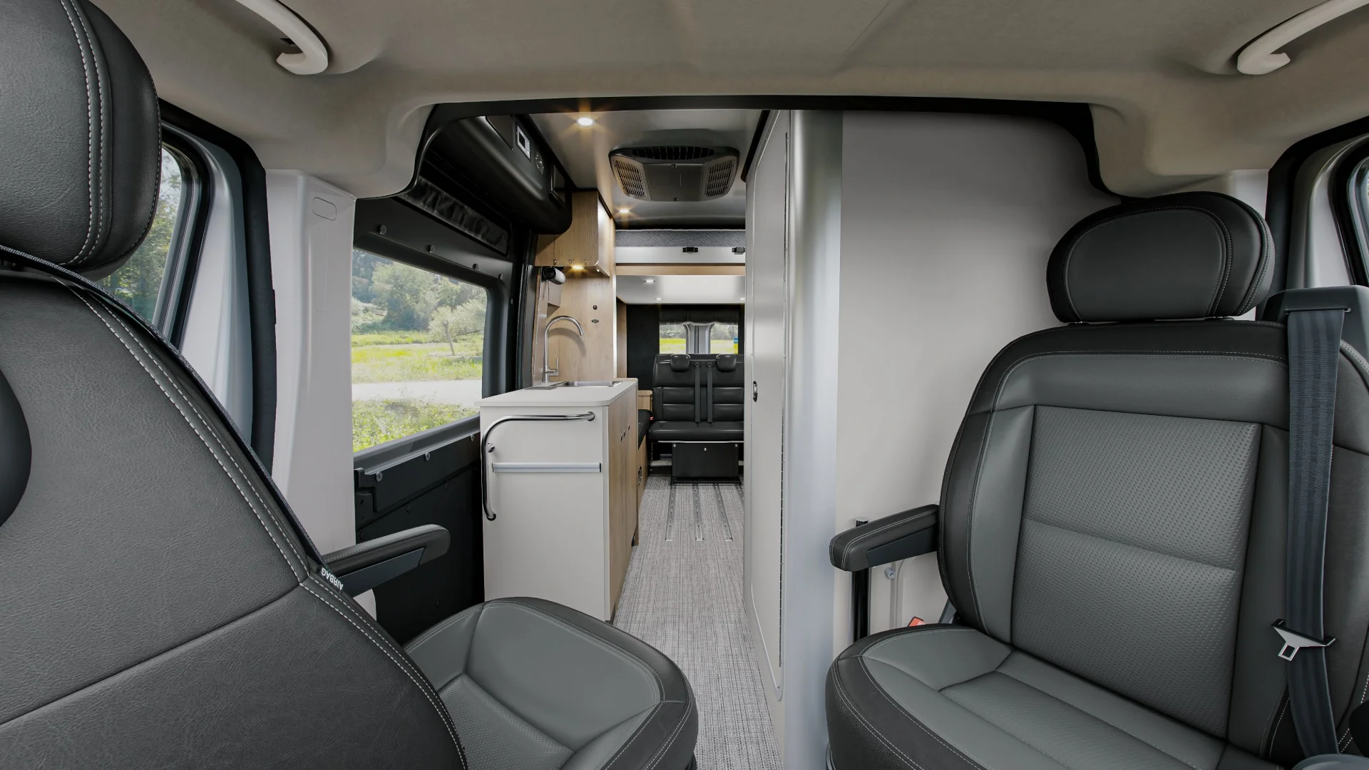 Luxury campervan interior with gray leather seats, compact kitchen, and seating area, featuring modern design and large windows.
