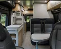 Interior of a modern camper van with sleek black seats, a compact kitchenette, wooden cabinets, and ambient lighting.