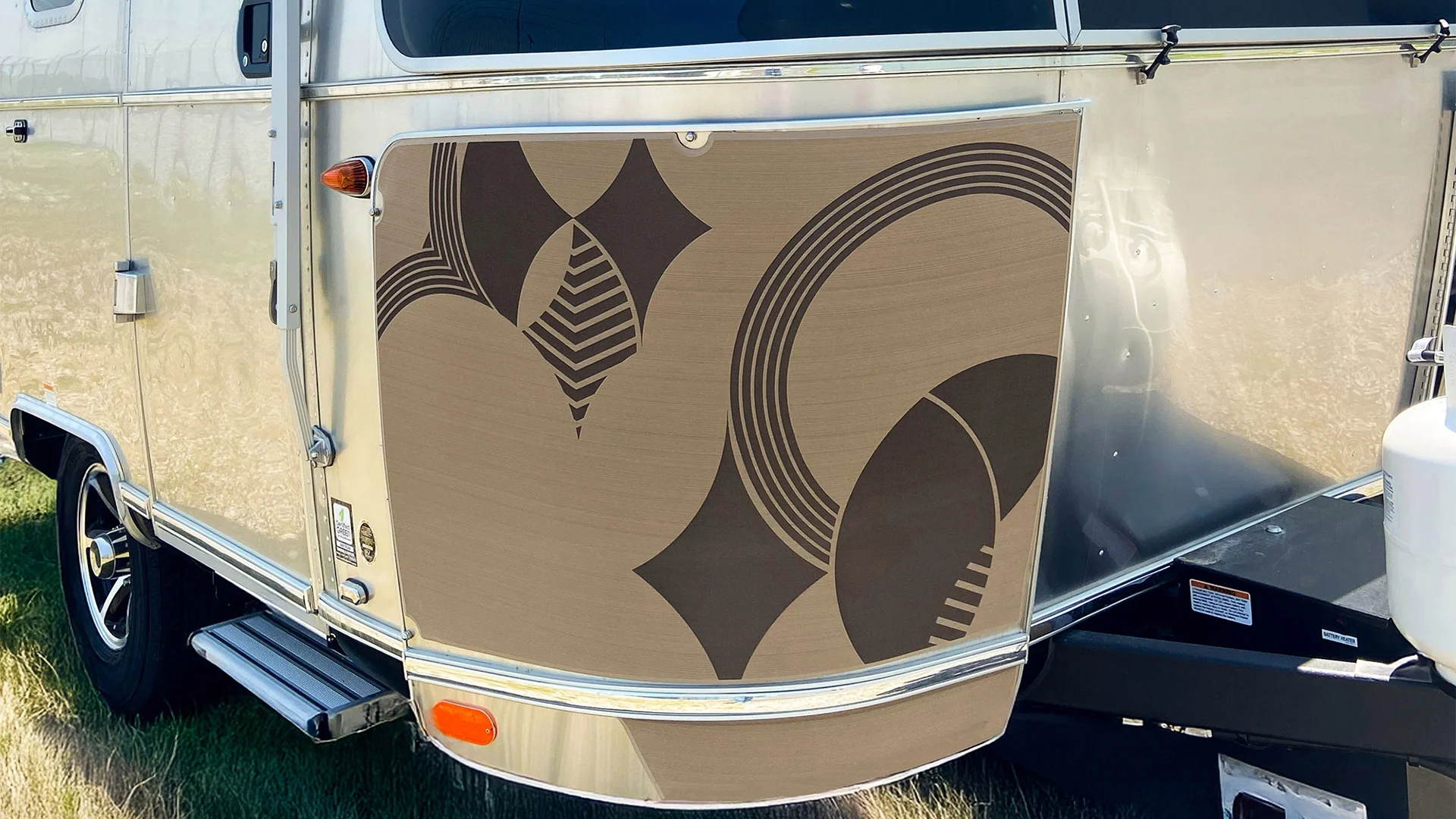 Close-up of a polished metal trailer with geometric patterns in brown and beige, featuring circles and diamond shapes.