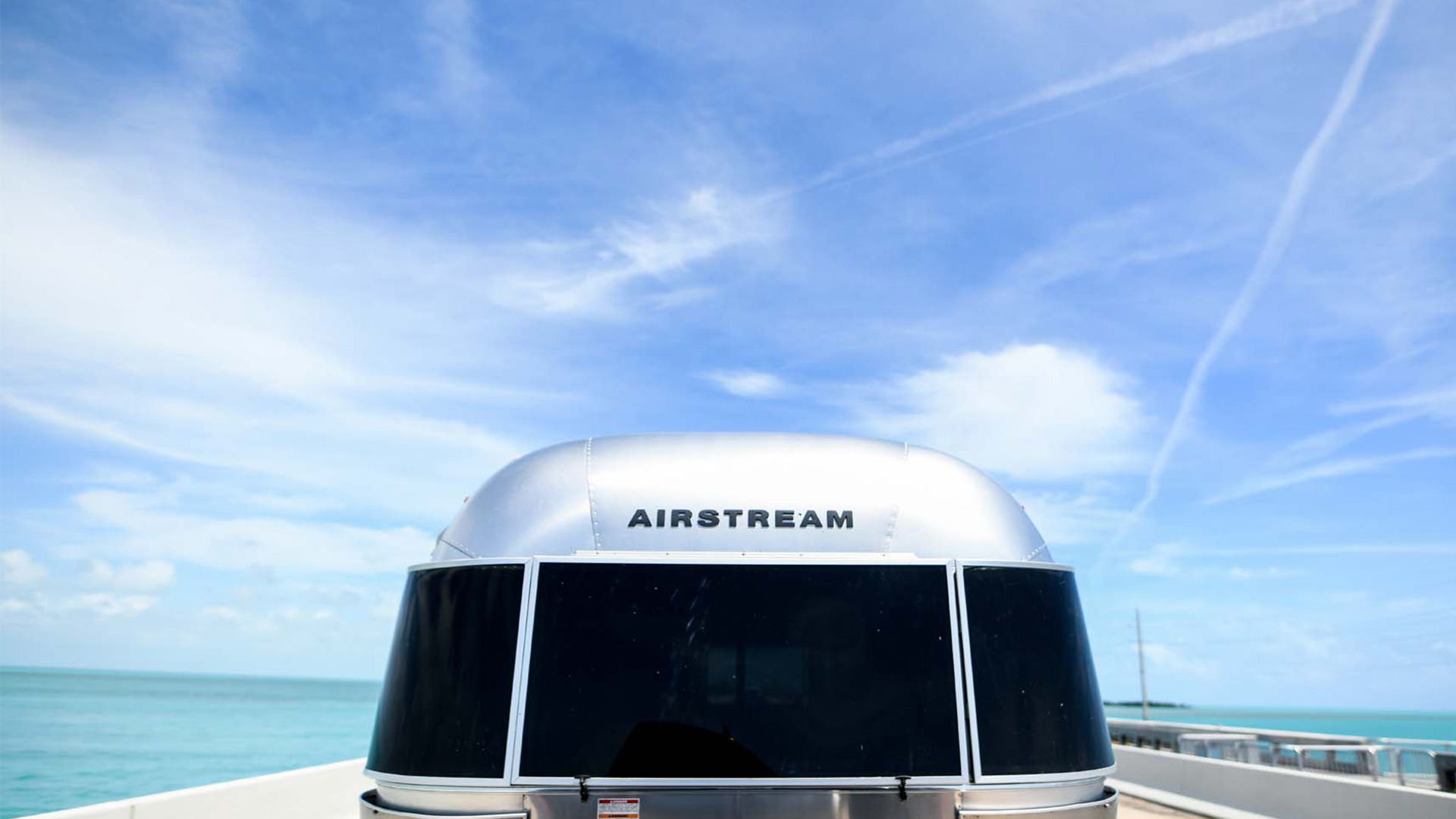 Silver Airstream trailer under a vibrant blue sky, with ocean visible at the horizon.
