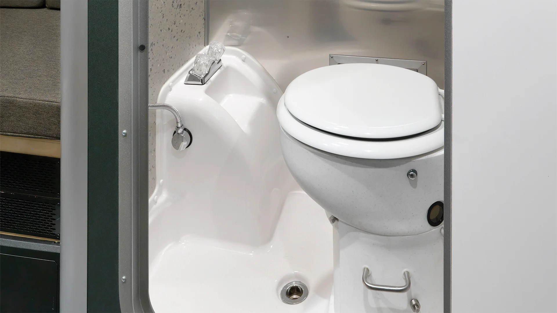 Compact RV bathroom featuring a white toilet, integrated sink, and a small hand shower, with a beige cushioned seat visible in the background.