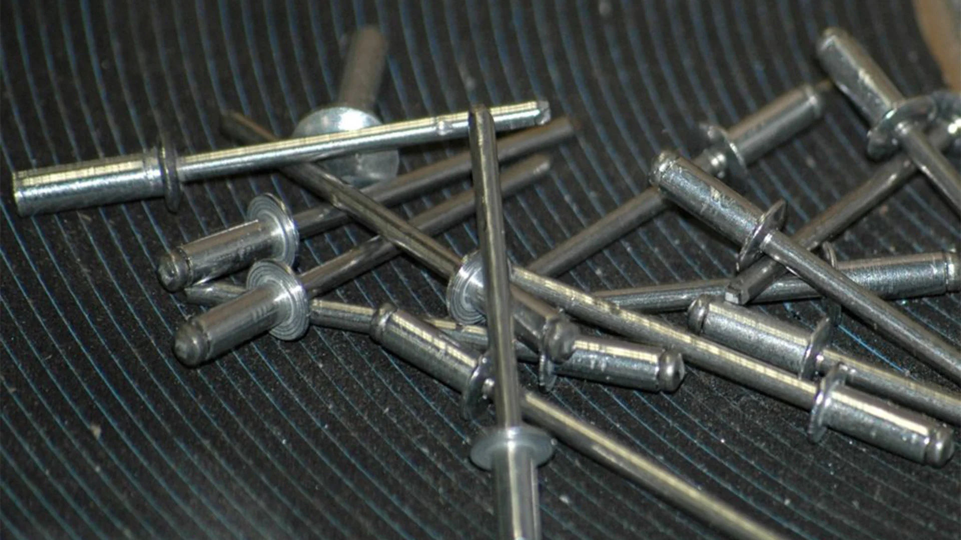 A pile of silver rivets scattered on a ridged black surface.