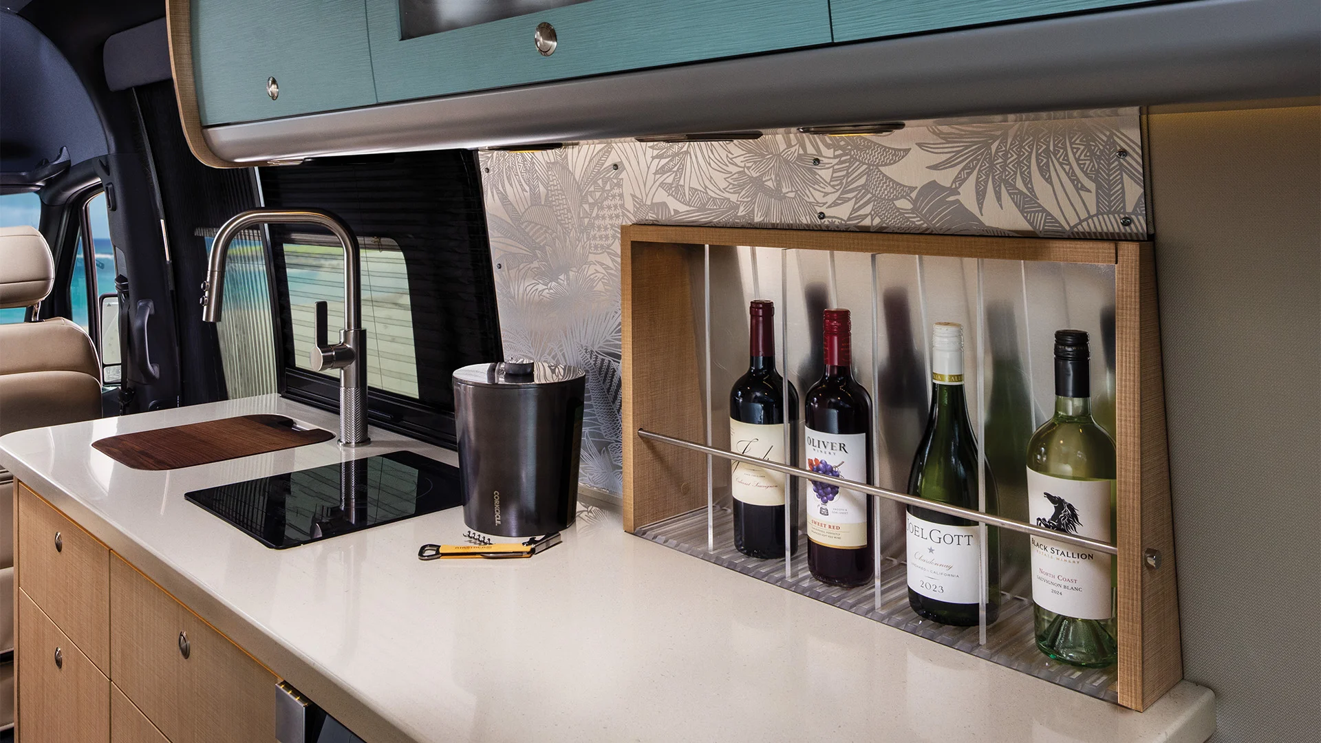 Modern campervan kitchen with a sleek countertop, wine bottle rack, sink, induction cooktop, and overhead cabinet.