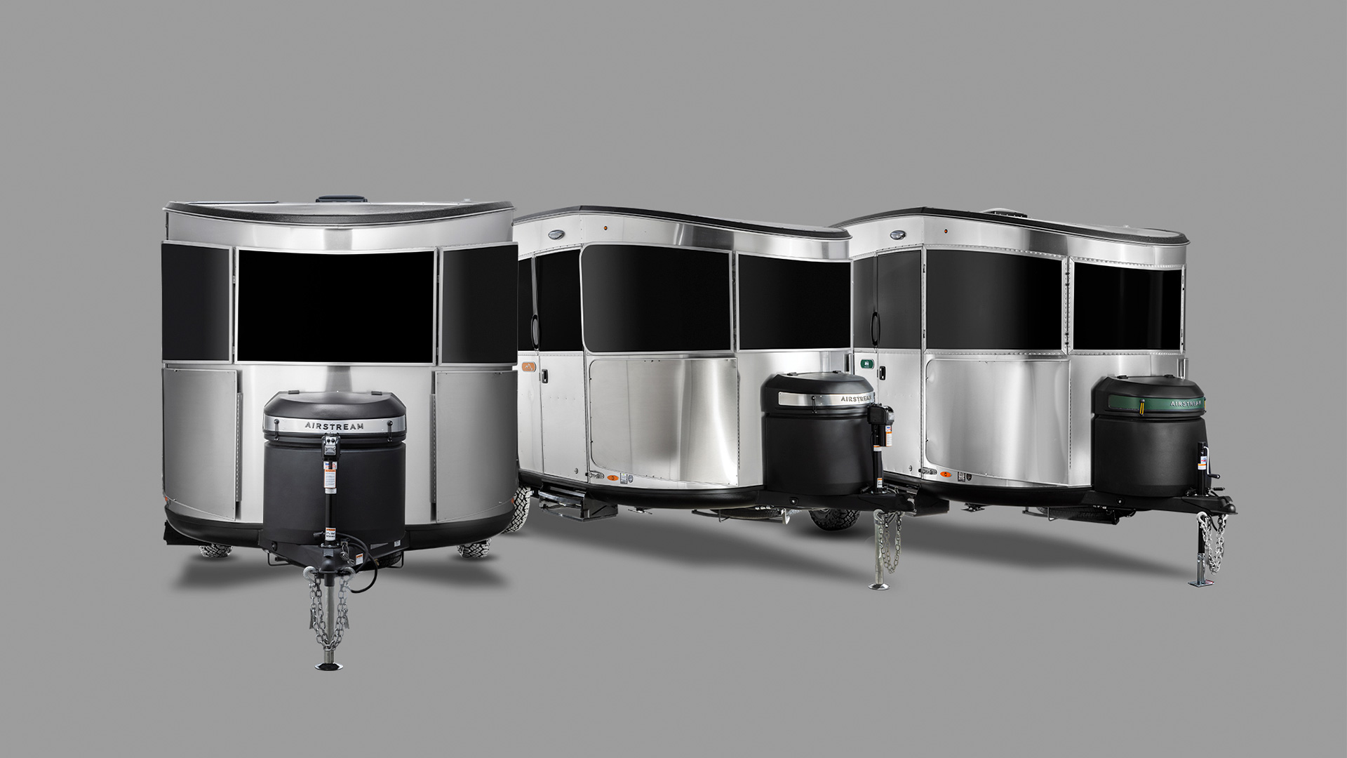 Three shiny, silver travel trailers with black fronts and attached hitches, arranged on a gray background.