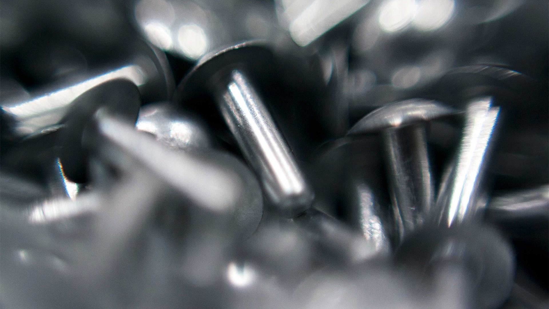 Close-up of shiny metal rivets with blurred edges, highlighting their smooth, cylindrical shape and reflective surfaces.