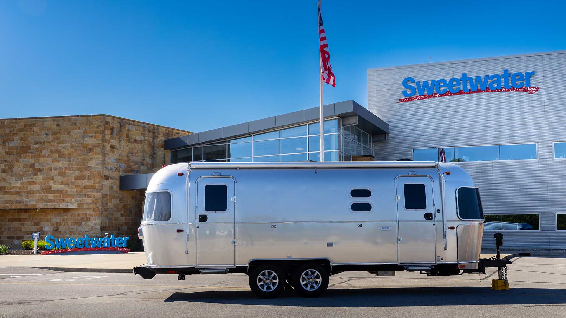 A sleek silver trailer parked outside a modern building with "Sweetwater" signage, under a clear blue sky with an American flag waving.