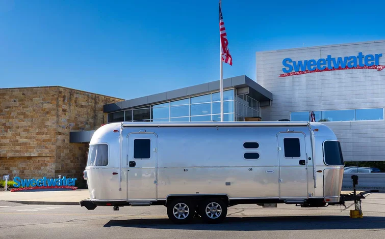 A sleek silver trailer parked outside a modern building with "Sweetwater" signage, under a clear blue sky with an American flag waving.