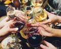 A group of people raise glasses of red and white wine in a celebratory toast, with a festive background setting.