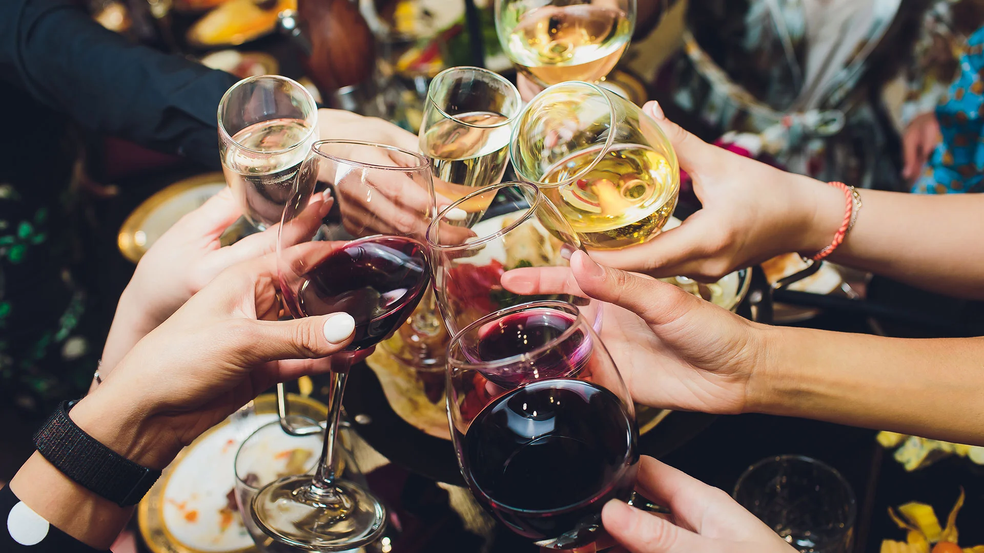 A group of people raise glasses of red and white wine in a celebratory toast, with a festive background setting.