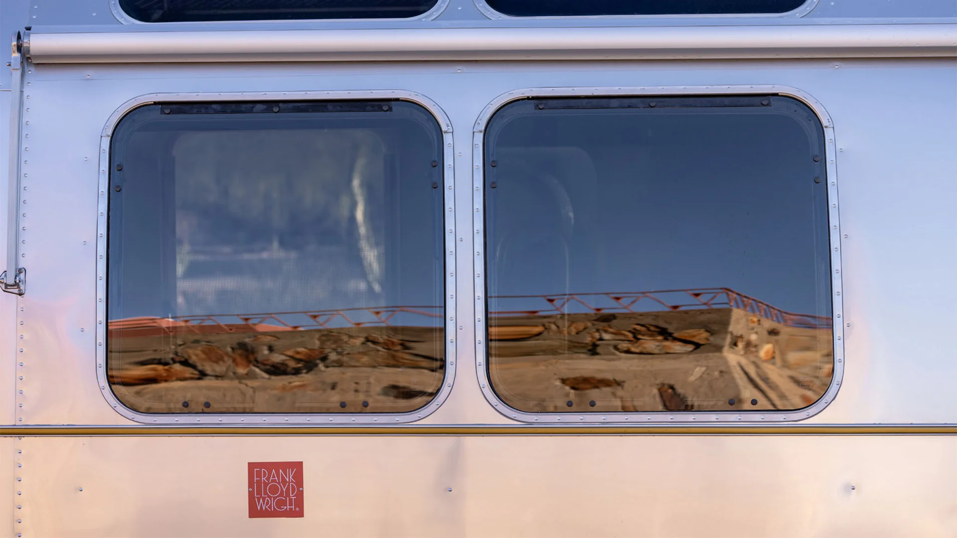 Reflection of a desert landscape with rocks and a blue sky in two rectangular windows on a shiny metallic surface.