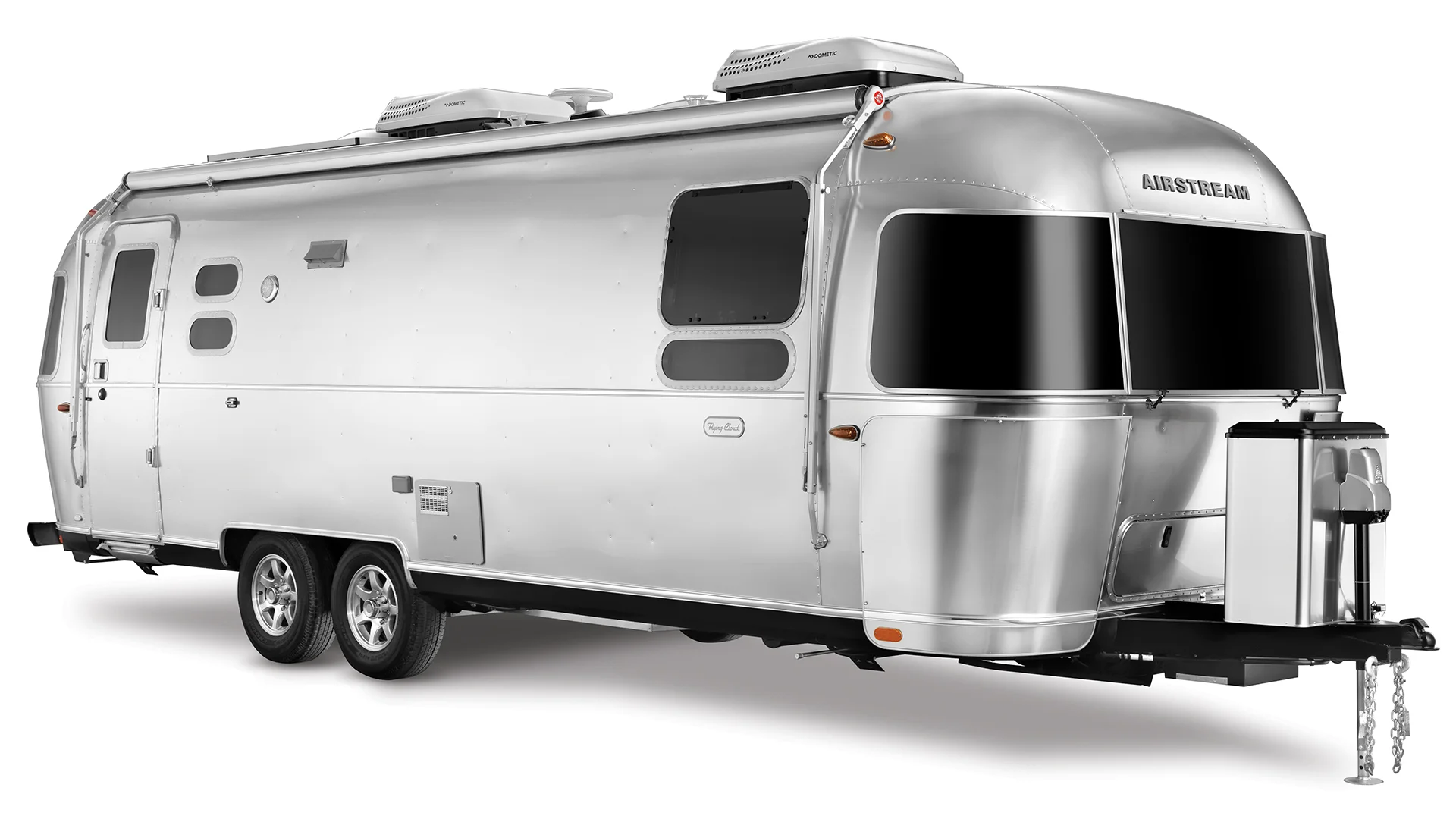 A shiny, silver Airstream travel trailer with two axles, rounded edges, large tinted windows, and roof-mounted air conditioners, shown on a white background.